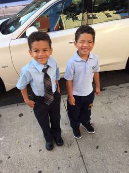 Two boys in school uniforms smiling on a sidewalk