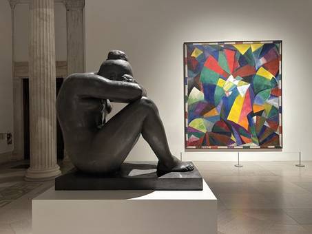 A bronze sculpture beside a colourful abstract painting in a museum