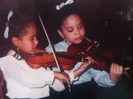 Two girls with bows in their hair playing violins